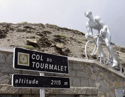 Col du Tourmalet summit signs at 2,115 m with the Giant cyclist statue above the stone wall